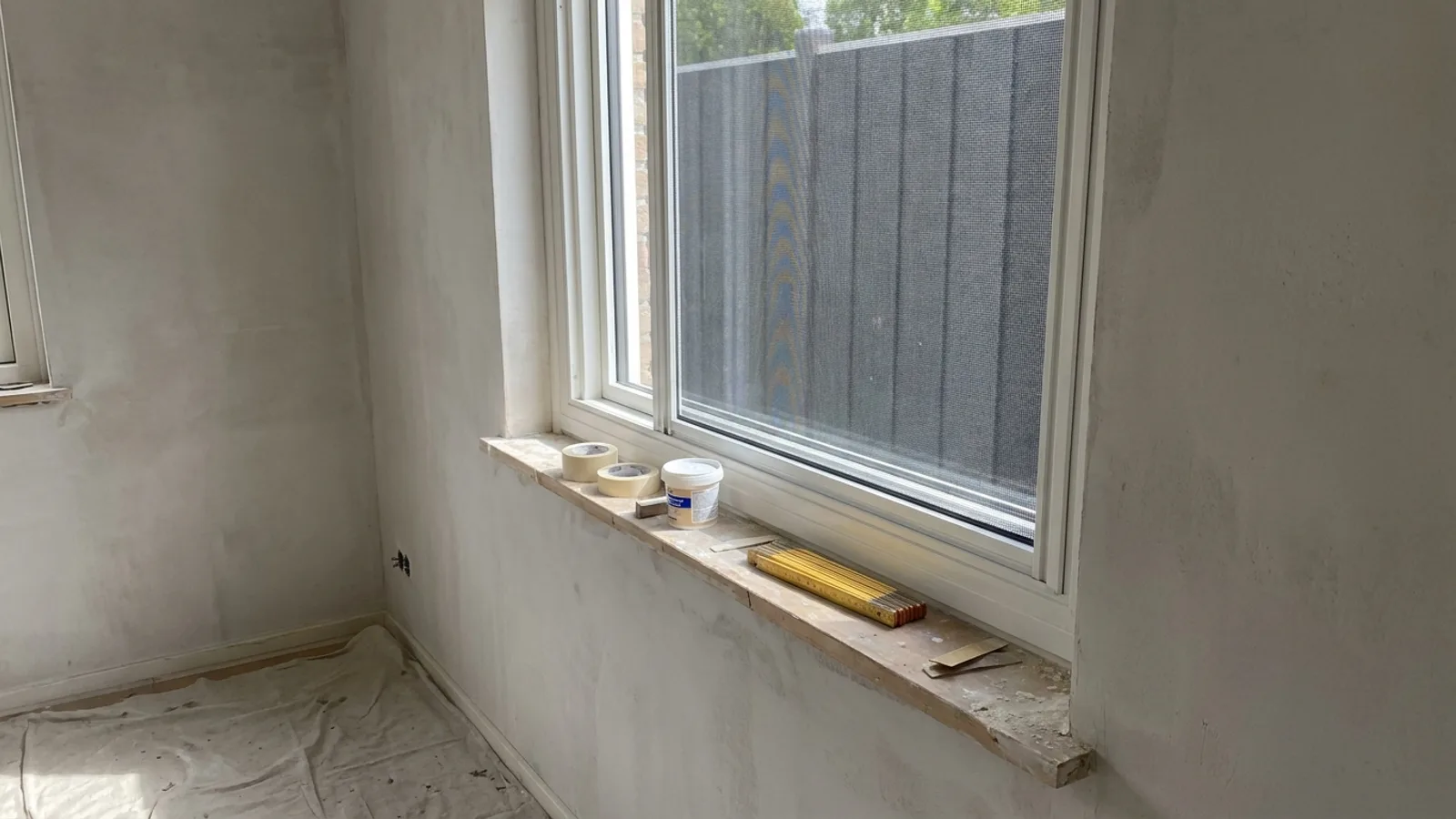 Neu eingebautes weißes Fenster mit feinem Insektenschutzgewebe im Rahmen in einem Raum während der Renovierung, Zollstock auf der Fensterbank