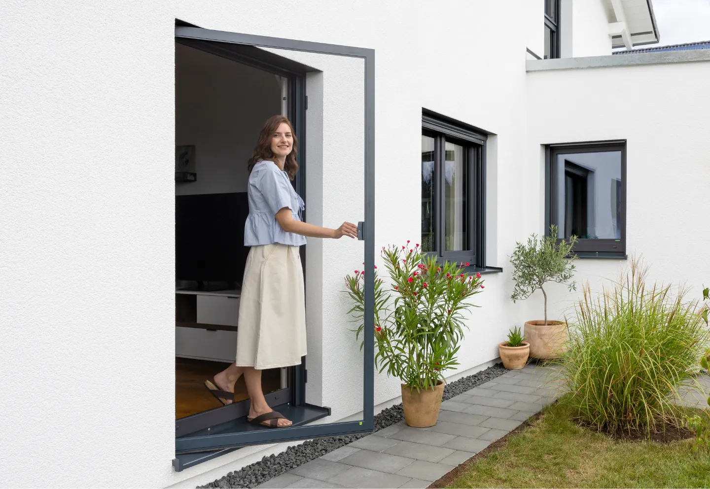 Frau öffnet Insektenschutztür an modernem Haus