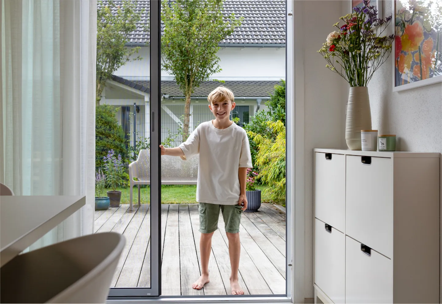 Offene Insektenschutz-Schiebeanlage an einer Terrassentür mit Blick auf Holzterrasse und Garten bei Tageslicht